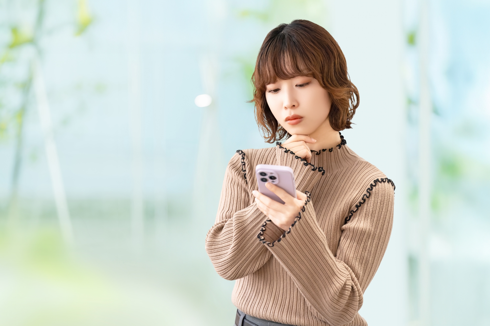 携帯電話を持ち考える女性のイメージ